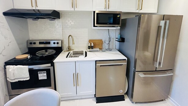 A compact kitchen with white cabinets, a stainless steel refrigerator, a microwave, a stove, and a dishwasher. - Cozy 1-Bedroom Apartment in the Heart of Grimsby (Grimsby)