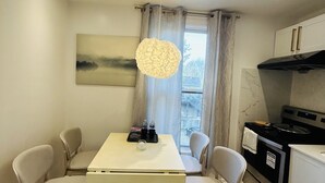 A compact kitchen with a dining table, chairs, a hanging light fixture, and a view of the outside through a window. - Cozy 1-Bedroom Apartment in the Heart of Grimsby (Grimsby)