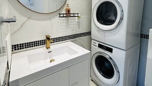 A modern bathroom with a white sink, a round mirror, and two stacked washing machines. - Cozy 1-Bedroom Apartment in the Heart of Grimsby (Grimsby)