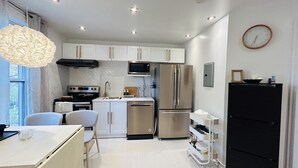A modern kitchen with white cabinets, stainless steel appliances, and a dining area with a white table and chairs. - Cozy 1-Bedroom Apartment in the Heart of Grimsby (Grimsby)