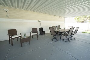 An outdoor patio with a covered seating area, a table, and chairs.