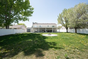 A two-story house with a covered patio and a circular stone feature in the yard.
