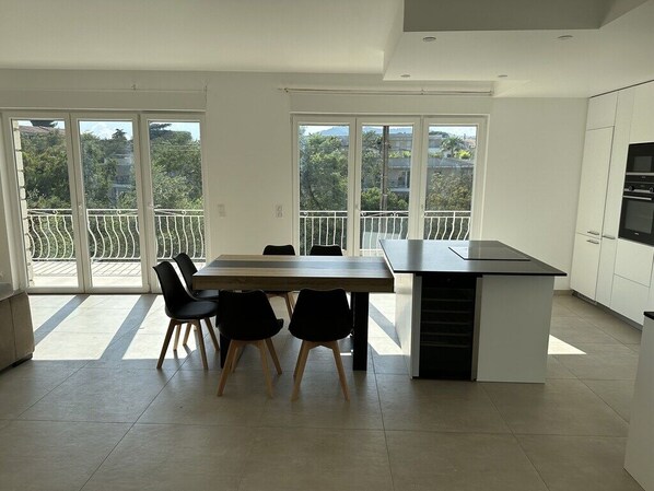 A modern kitchen with a dining area, large windows, and a balcony.