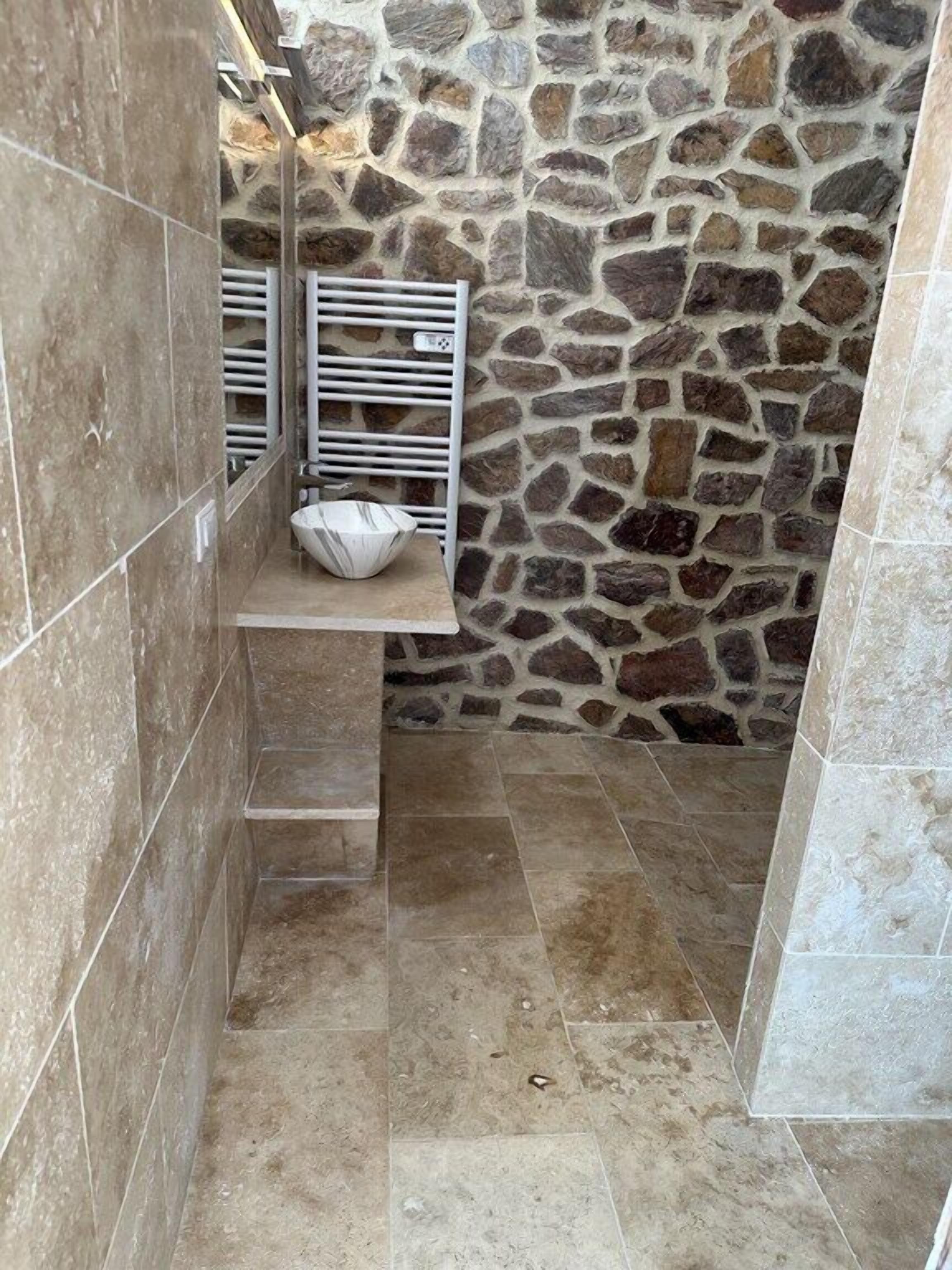Un bany amb parets de pedra, terra de rajola i un lavabo blanc amb una tassa.