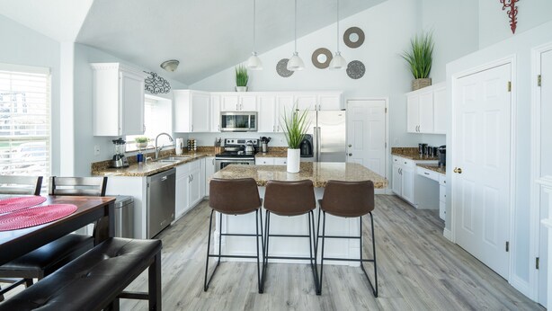 A modern kitchen with white cabinets, a central island with bar stools, stainless steel appliances, and decorative wall plates.