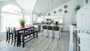 A modern kitchen with white cabinets, a dining area with a wooden table and chairs, and a staircase leading to another level.