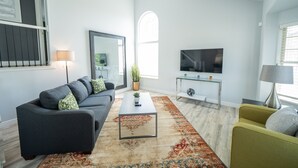 A modern living room with a grey sofa, a green armchair, a coffee table, and a TV on a stand.