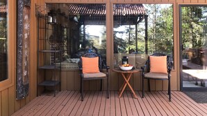 Una terraza de madera con dos sillas y una mesita, un adorno en la pared y vistas a los árboles circundantes.