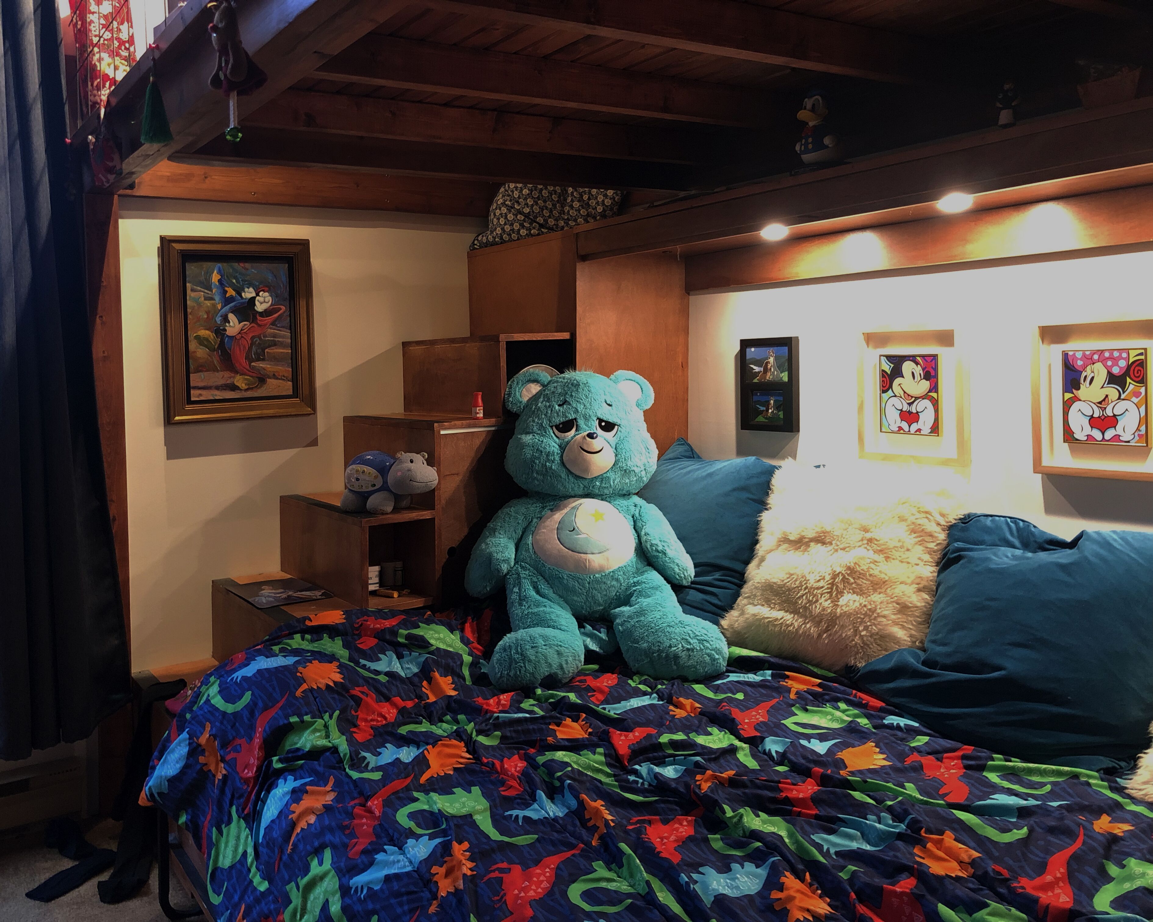 Une chambre confortable avec un lit, un grand ours en peluche bleu et divers tableaux encadrés accrochés aux murs.