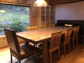 A wooden dining table with six chairs, a cabinet with glass doors, and a view of the outdoors through a window. - Misty Haven Main House (Victoria)