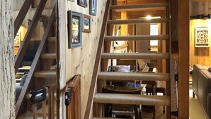 Una escalera de madera con barandilla que lleva a una habitación con un piano y una chimenea.