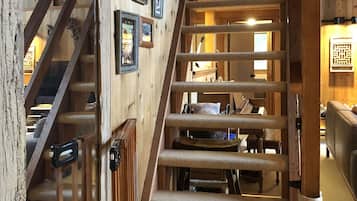 A wooden staircase with a handrail, leading to a room with a piano and a fireplace.