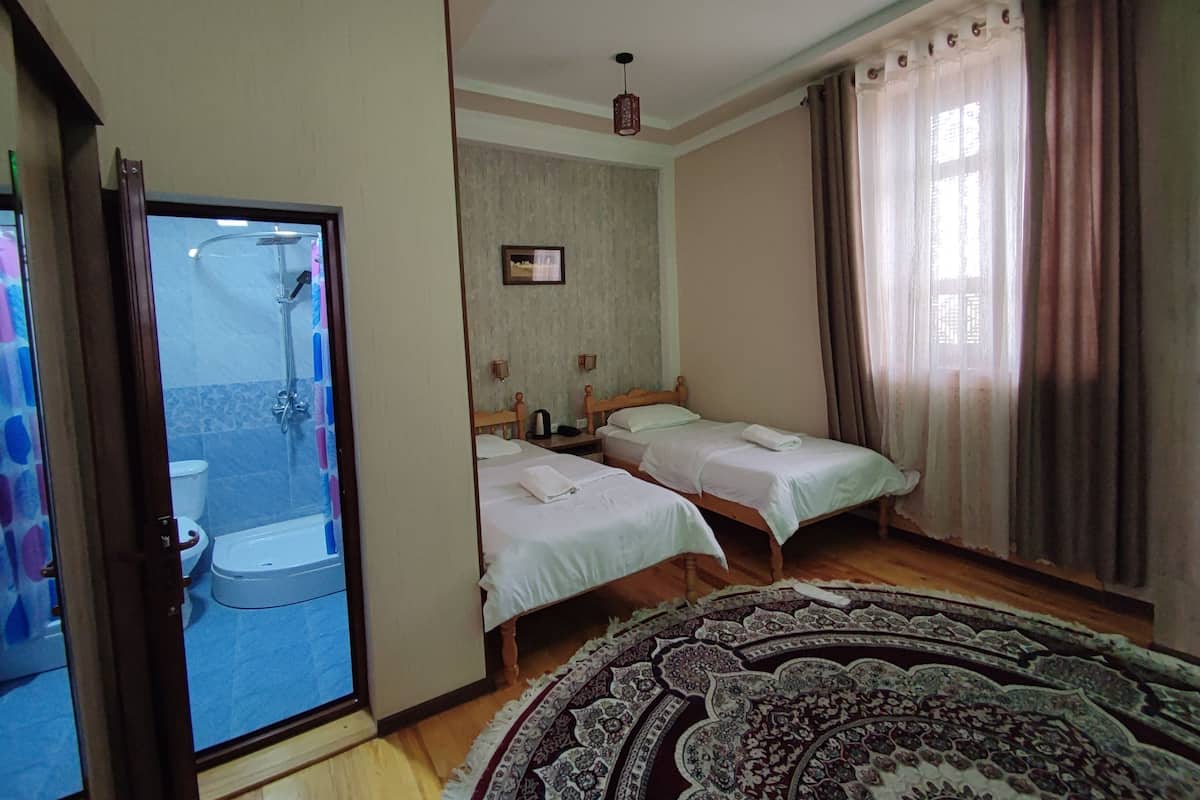 Une chambre d’hôtel avec deux lits, une douche, des toilettes et une grande fenêtre avec des rideaux.