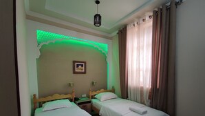 A room with two single beds, a nightstand, a wall-mounted picture, and a green decorative light. - Naqshband Craft Center & Hotel (Bukhara)
