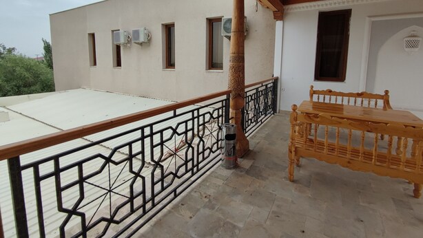 A balcony with a wooden table and chairs, a metal railing, and air conditioning units on the building facade. - Naqshband Craft Center & Hotel (Bukhara)