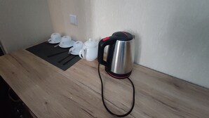 A kitchenette with a stainless steel kettle, white cups, and a black mat on a wooden countertop. - Naqshband Craft Center & Hotel (Bukhara)