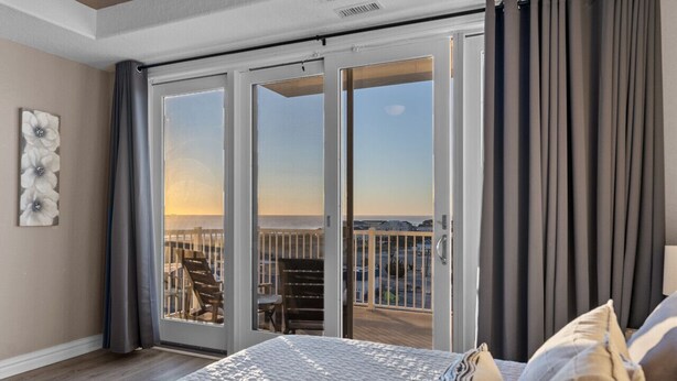 A bedroom with a large bed, a view of the balcony, and a sliding glass door. - Beachfront Penthouse!  4Bd/3Bth (Virginia Beach)