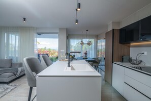 Relax in a stylish space with a central kitchen island, comfortable sofas, and a dining table, offering a view of the surrounding landscape.
