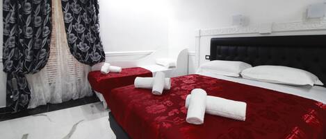 A hotel room with two beds, red bedding, white headboards, and a large window with black and white floral curtains.