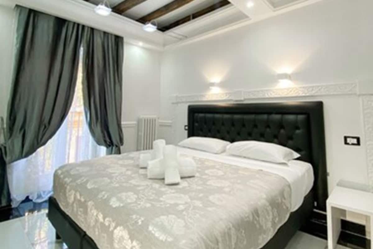 Slaapkamer met een groot bed, houten balken in het plafond, een radiator en een klein nachtkastje.