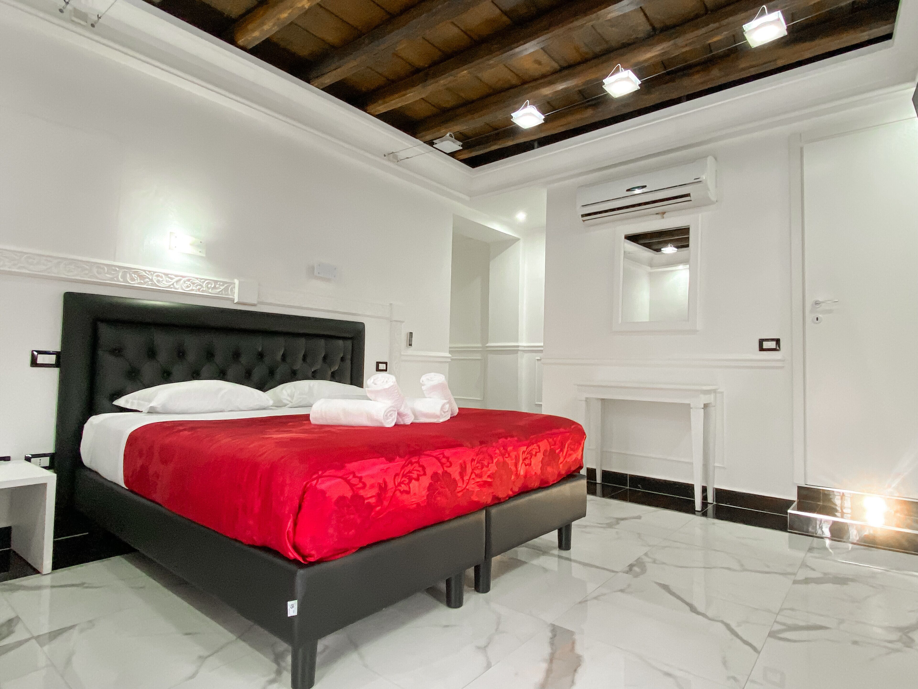 Un dormitorio moderno con una cama grande, paredes blancas, techo de madera y suelo de mármol.