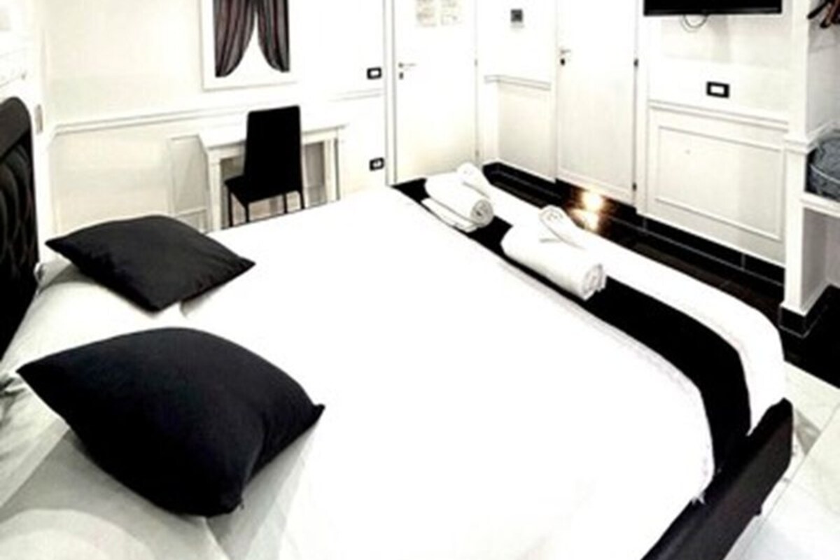A hotel room with a bed, a desk, a chair, a television, and a wardrobe.