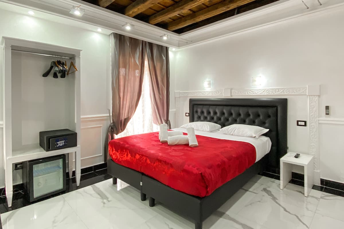 A modern bedroom with a large bed, a built-in wardrobe, a small bedside table, and a ceiling with exposed beams.