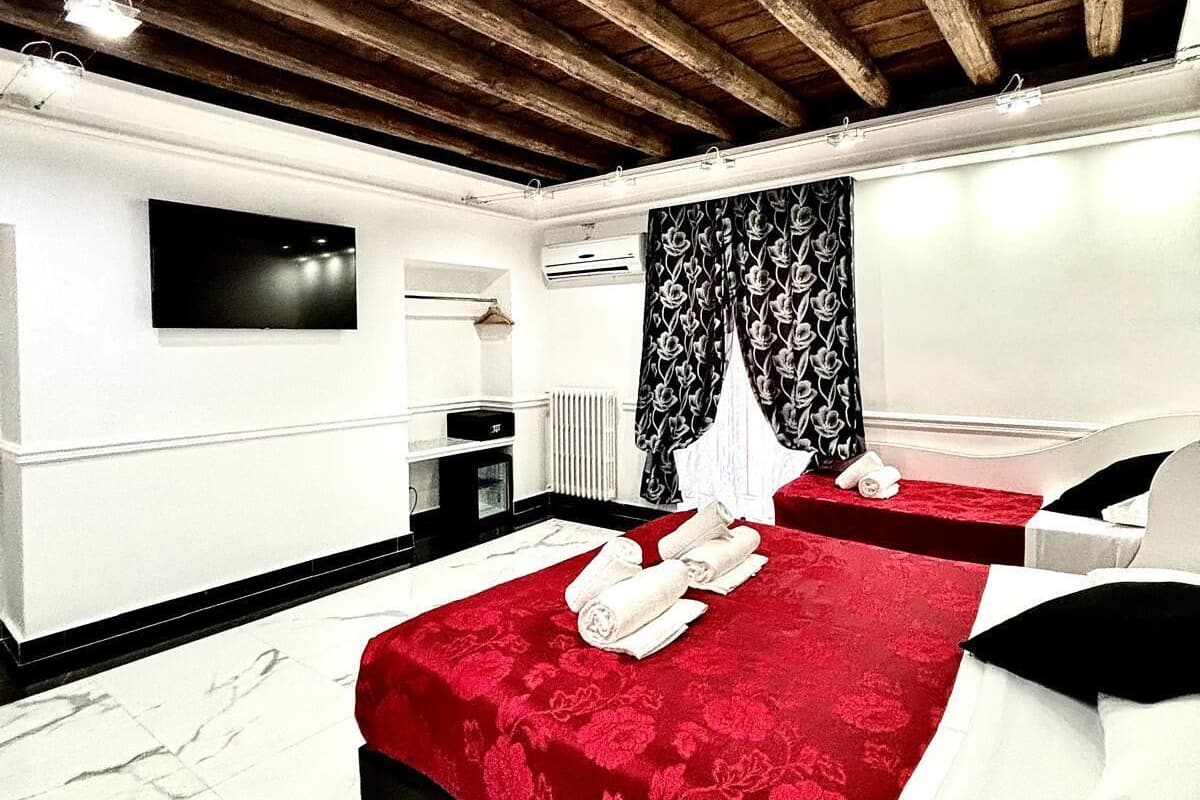 A hotel room with a red carpet, a large bed with white linens, a flat-screen TV mounted on the wall, and a wooden ceiling.