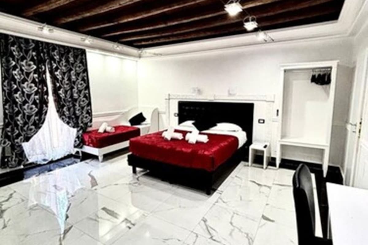 A hotel room with two beds, a marble floor, wooden ceiling beams, and a white wall with a black and white patterned curtain.