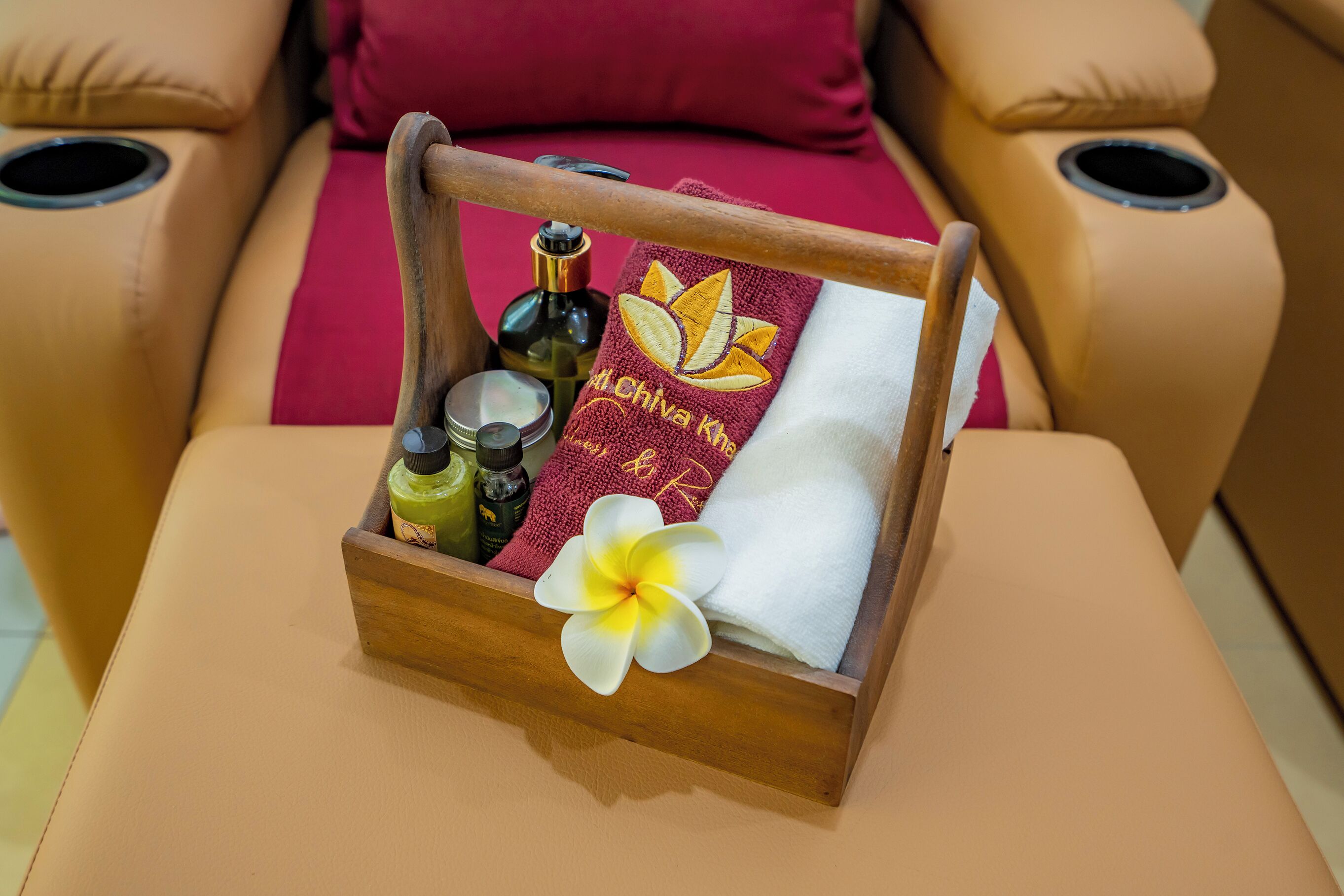 Ein Massagesessel mit einem Holznachttisch, auf dem ein Handtuch, eine Flasche und eine Blume liegen.