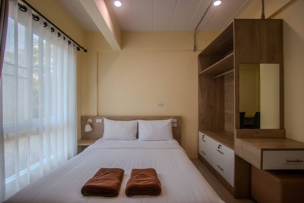 A hotel room with a bed, two towels, a nightstand, a mirror, and a wardrobe.