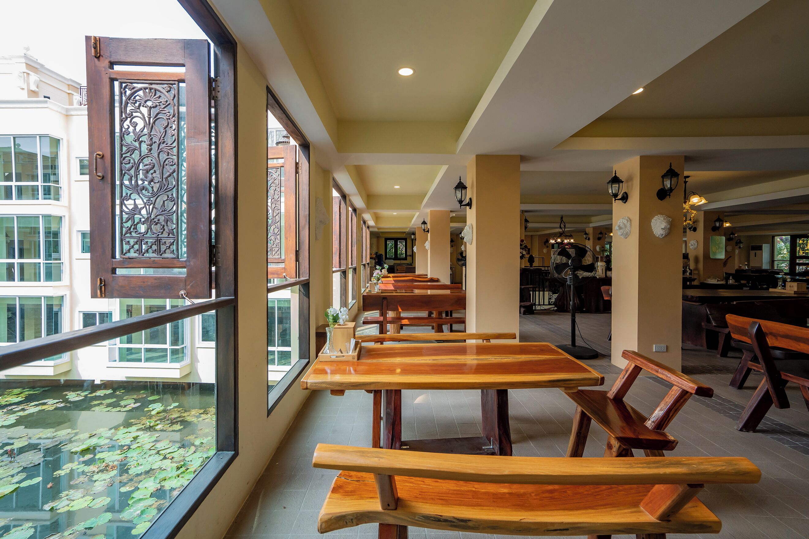 A restaurant with wooden tables and benches, large windows with decorative metal grilles, and a view of a building with multiple windows.