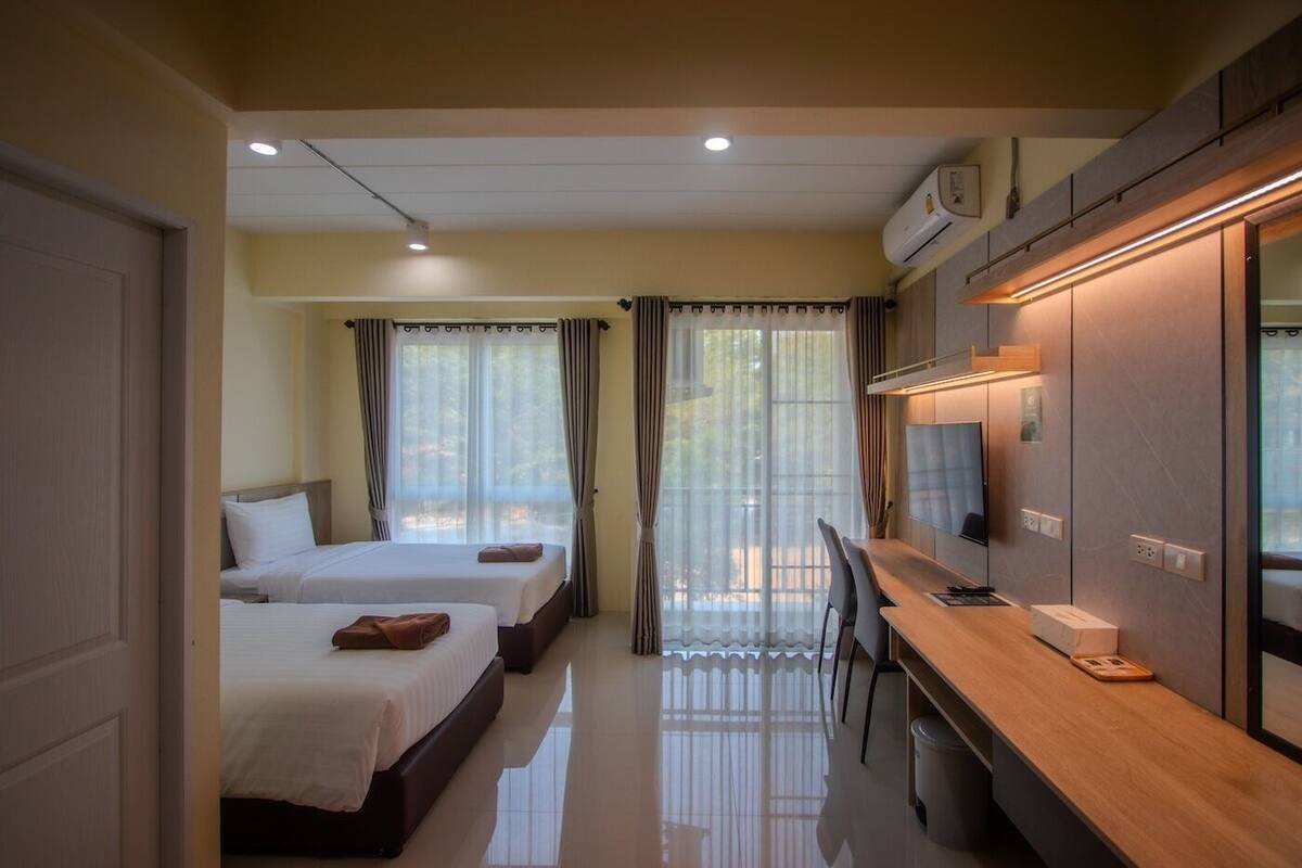 A hotel room with two beds, a desk, a TV, and an air conditioning unit.