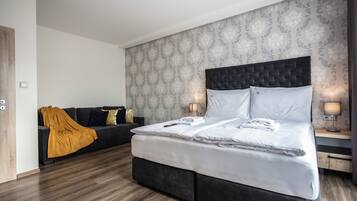A modern hotel room with a large bed, a sofa, and a patterned wallpaper.