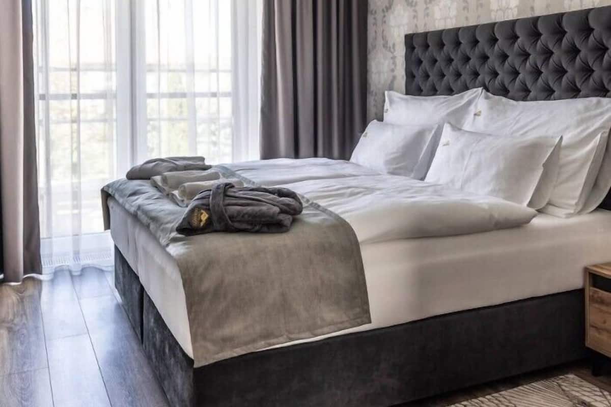 A neatly made bed with a dark headboard, white bedding, and a grey throw blanket.