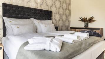 A neatly made bed with white linens and a grey throw blanket, a dark tufted headboard, and a nightstand with a vase of dried flowers.