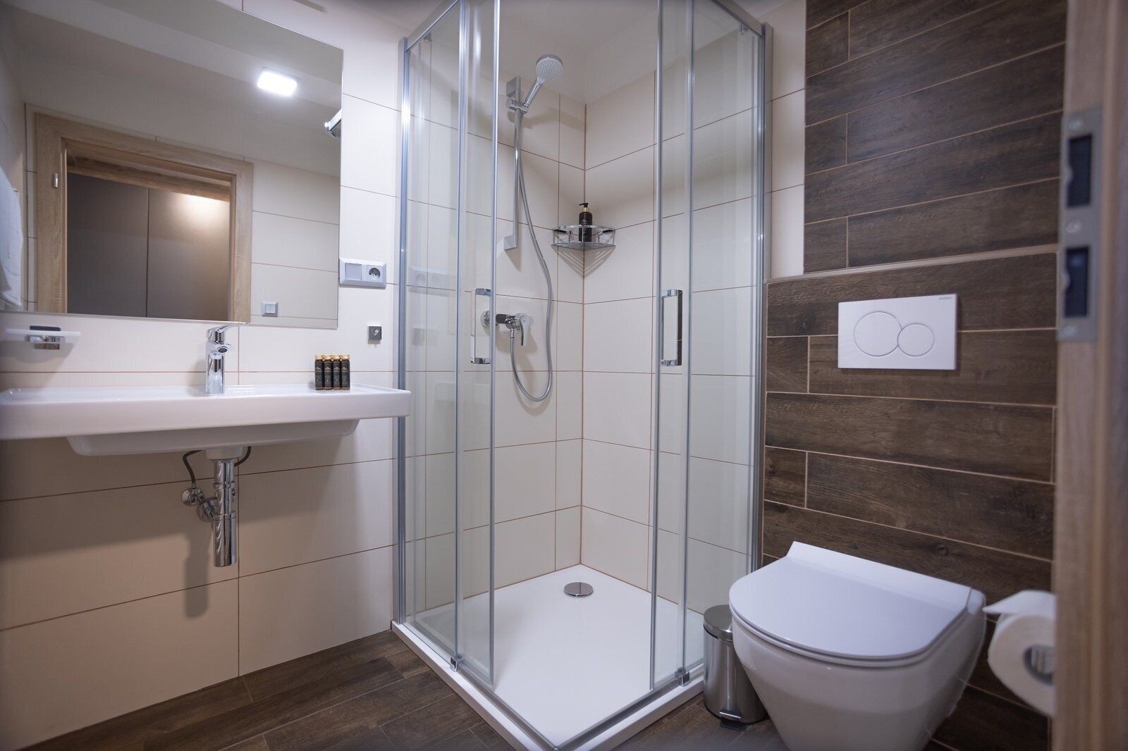 Un baño moderno con ducha de vidrio, lavamanos blanco y retrete.