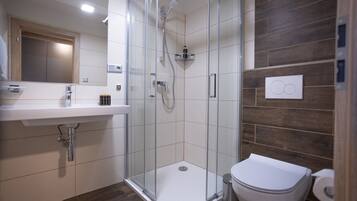 Un baño moderno con ducha de vidrio, lavamanos blanco y retrete.