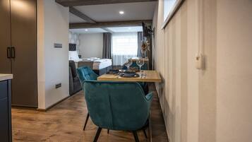 Ett modernt hotellrum med trägolv, turkosa stolar, ett trämatbord och en säng med en grå sänggavel.