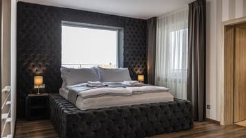 Un dormitorio moderno con una cama grande, paneles de pared oscuros, una ventana con cortinas y suelo de madera.