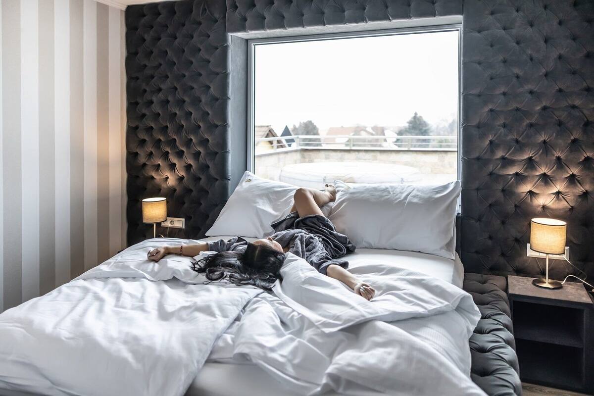 A bedroom with a tufted headboard, a large window, and bedside lamps.