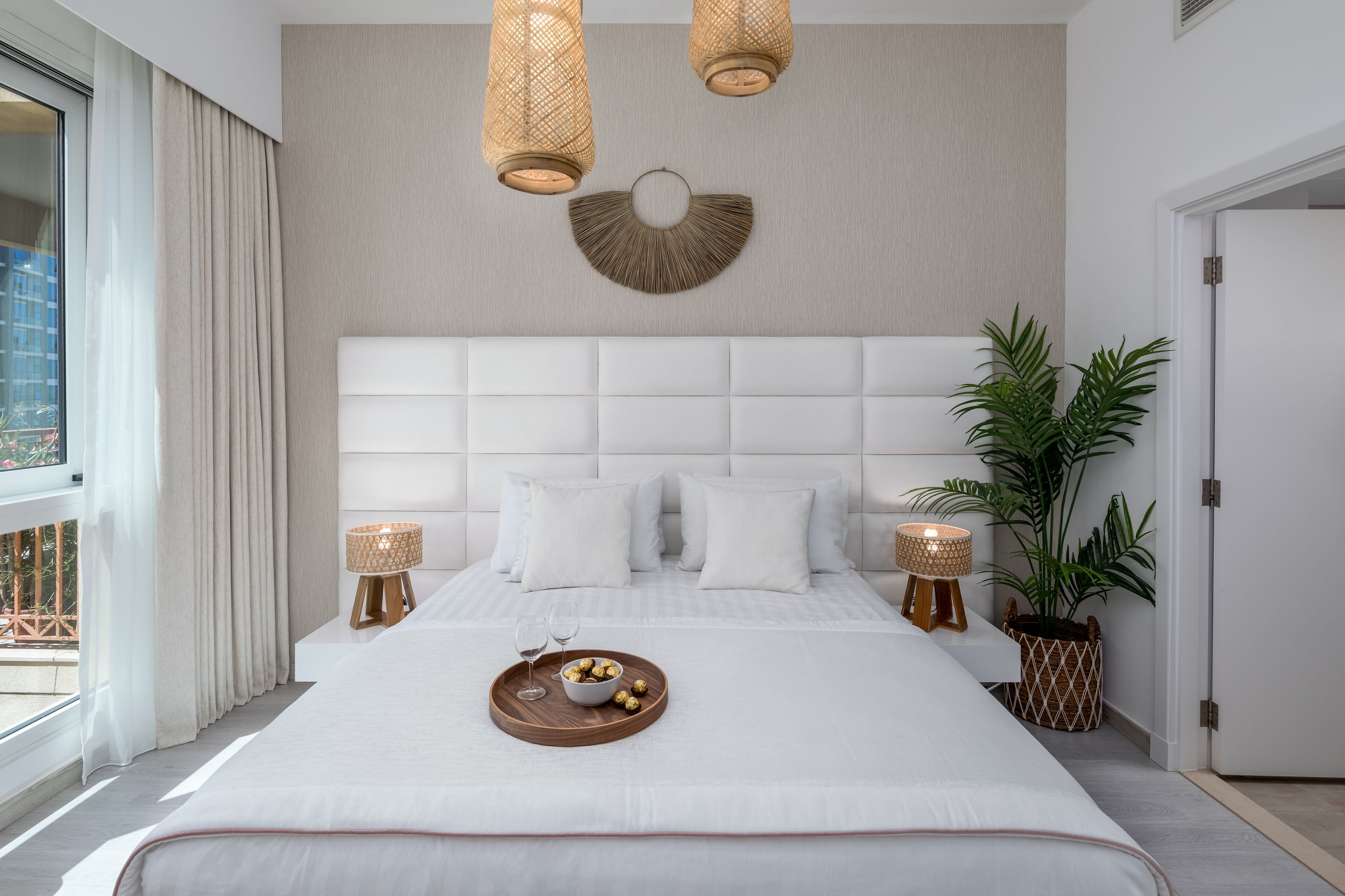 Een moderne hotelkamer met een groot bed, twee nachtkastjes, een wandlamp, een kamerplant en uitzicht op het omliggende landschap.