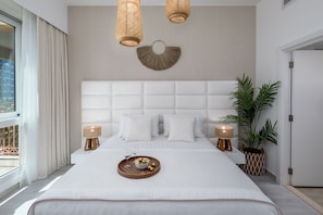 Ein modernes Hotelzimmer mit einem großen Bett, zwei Nachttischen, einer Wandleuchte, einer Topfpflanze und Blick ins Freie.