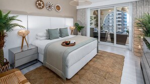 Un dormitorio moderno con una cama grande, mesitas de noche, una lámpara colgante y vistas de la ciudad a través de ventanales de piso a techo.