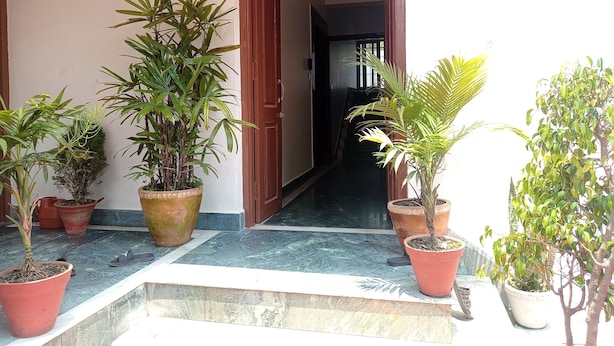 A covered entrance with potted plants, a wooden door, and a tiled floor leading to an interior space. - Janaki House (Burhanilkantha)