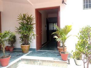Un acceso cubierto con plantas en macetas, una puerta de madera y un piso de baldosas que conducen a un espacio interior.