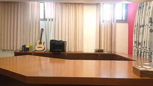 A room with a wooden desk, a guitar, a printer, and a window with curtains. - Janaki House (Burhanilkantha)