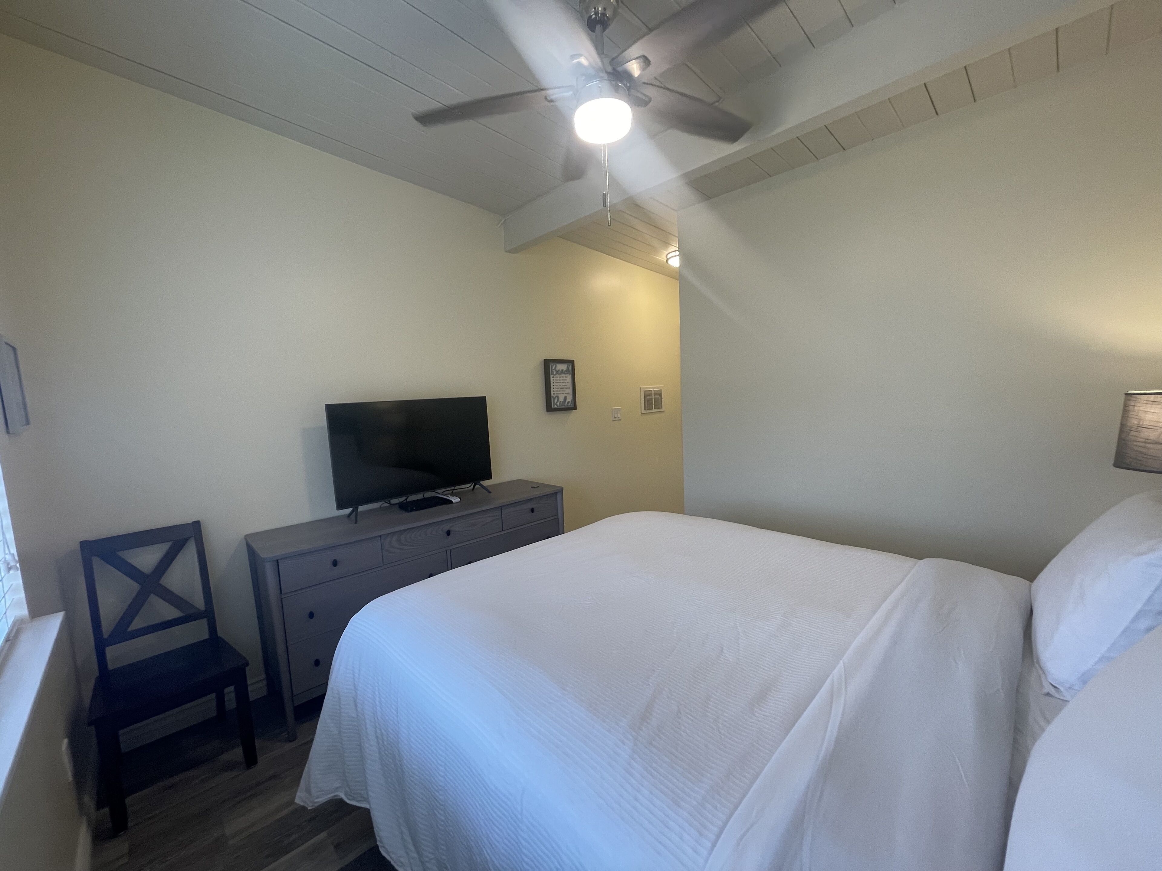 A bedroom with a bed, a dresser, a television, and a ceiling fan.