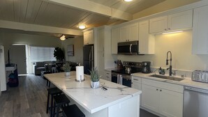 A modern kitchen with white cabinets, a marble countertop, and a central island with bar stools. - Ultimate Beach Vacation in the Heart of Carlsbad  (Carlsbad)