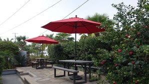 An outdoor patio area with stone flooring, picnic tables, and red umbrellas. - Ultimate Beach Vacation in the Heart of Carlsbad  (Carlsbad)